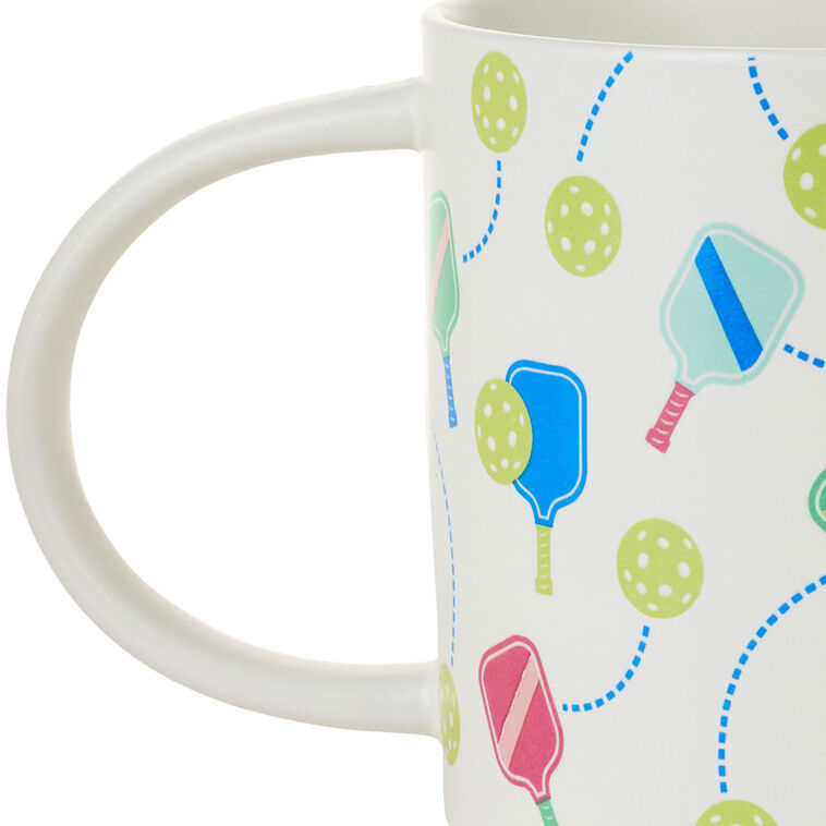 White ceramic pickleball mug with colorful paddle and ball icons, oversized handle, and stackable recessed base