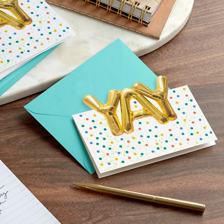 White note cards with gold balloon-style “YAY” lettering, confetti dots, and die-cut front, packaged in kraft wrap.
