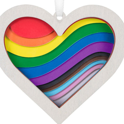 Heart-shaped rainbow papercraft ornament in a whitewashed wood frame with “Love Wins” ribbon for LGBTQIA holiday celebration.