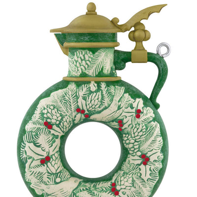 Green beer stein ornament with vintage wreath design, holly, and pinecones; features a gold lid and elegant holiday detailing.