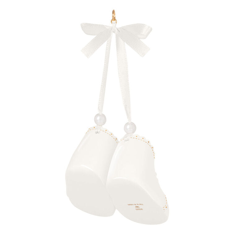 White porcelain baby booties ornament with 14K gold accents and satin ribbon bow, marked for baby’s 1st Christmas 2025.