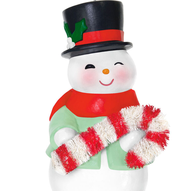 Porcelain snowman ornament in festive coat, scarf, and top hat holding a bottlebrush candy cane