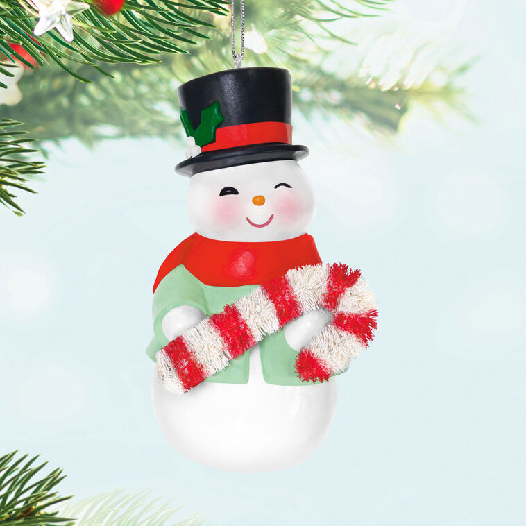 Porcelain snowman ornament in festive coat, scarf, and top hat holding a bottlebrush candy cane