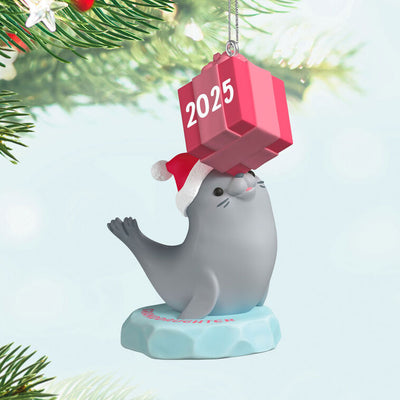 2025 Christmas ornament with gray seal in Santa hat on iceberg, balancing pink present on nose, festive design

