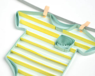 Quilled baby card with onesies, bibs, and hats hanging from a clothesline. A handmade card perfect for welcoming a newborn.