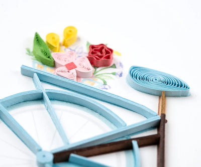 Hand-quilled greeting card featuring a blue bicycle with a flower-filled basket and green border, perfect for cheerful occasions.