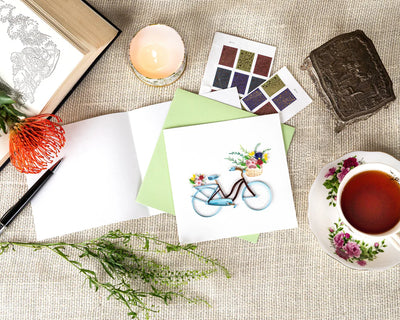 Hand-quilled greeting card featuring a blue bicycle with a flower-filled basket and green border, perfect for cheerful occasions.