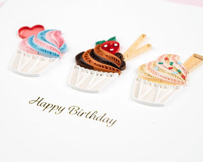 Quilled birthday card with three cupcakes topped in colorful frosting, candy decor, and gold “Happy Birthday” script—fun and festive.