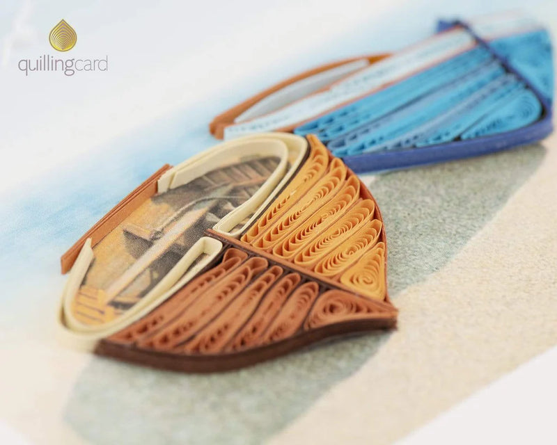 Quilled card with orange and blue canoes resting on a sandy beach, with ocean waves and birds in the background—evoking calm and connection.