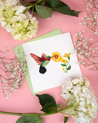 Handcrafted quilled card showing a hummingbird sipping nectar from vibrant yellow flowers, symbolizing beauty, energy, and joy.