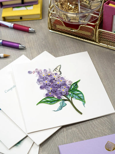 Quilled card with lilac flowers and green leaves on a watercolor background with a swallowtail butterfly