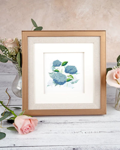Quilled card showcasing a cluster of vibrant blue hydrangeas with green leaves, delicately handcrafted on a soft white background.