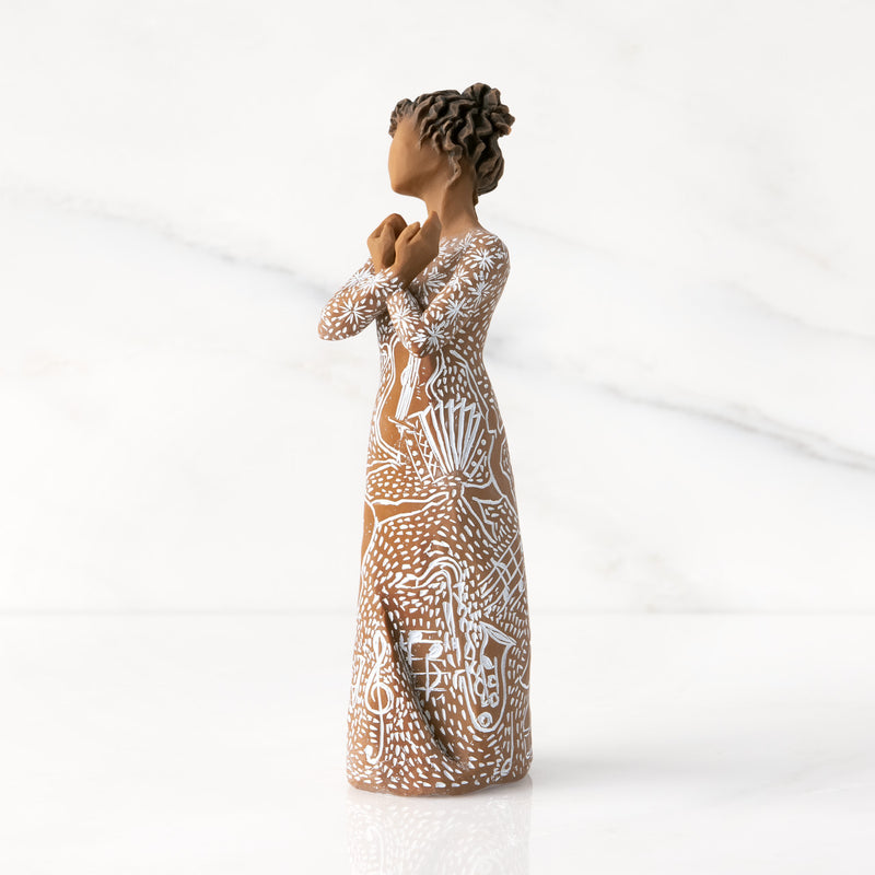 Willow Tree Music Speaks figurine with darker skin wearing a dress carved with musical symbols and dancing figures.