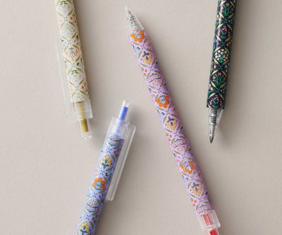 Set of four Rifle Paper Co. Estee gel pens with floral designs and colored inks in blue, black, red, and metallic gold.