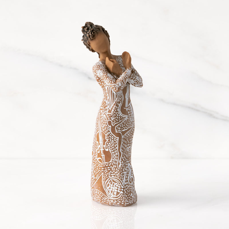 Willow Tree Music Speaks figurine with darker skin wearing a dress carved with musical symbols and dancing figures.