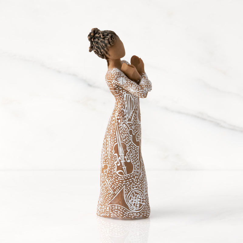 Willow Tree Music Speaks figurine with darker skin wearing a dress carved with musical symbols and dancing figures.
