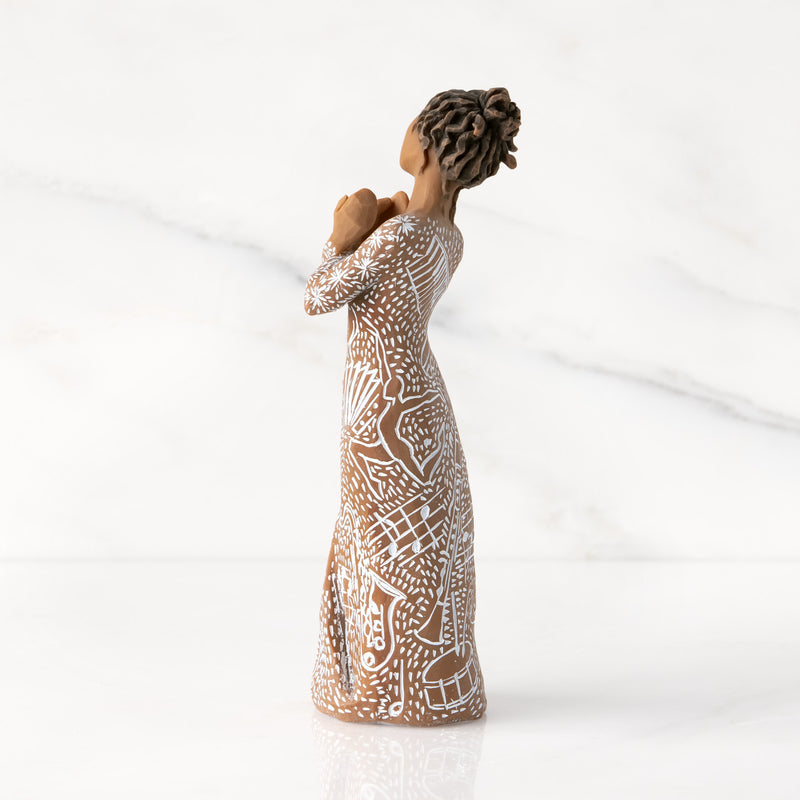 Willow Tree Music Speaks figurine with darker skin wearing a dress carved with musical symbols and dancing figures.