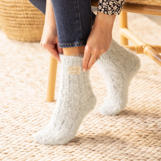 Cream fuzzy women’s socks with rubber grippers on the soles, ultra-soft and cozy, part of the Demdaco Giving Collection.