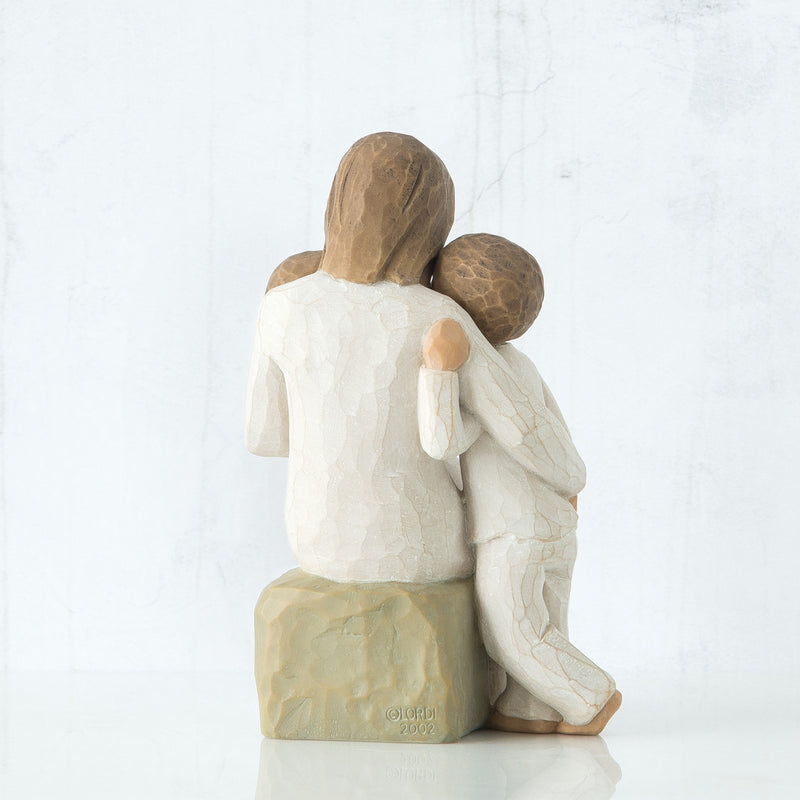 Willow Tree Quietly figurine of mother seated with toddler in arms and older child standing beside her, all in cream outfits.