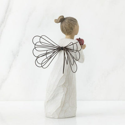 The figurine features an angel with outstretched arms clutching a bright red apple