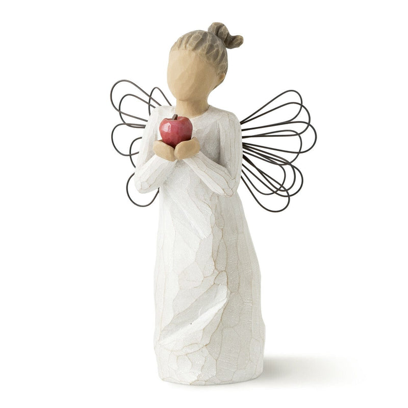 The figurine features an angel with outstretched arms clutching a bright red apple